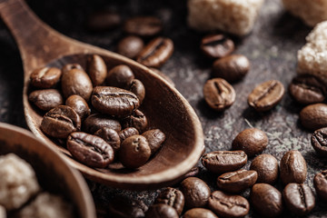 Coffee beans in wooden spoon on dark textured background.