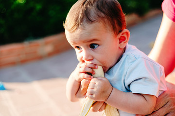 6 month old baby nibbling a banana in his garden.