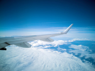 Fototapeta premium The wings of the plane during the flight look from the passenger window. There are white clouds in the blue sky.