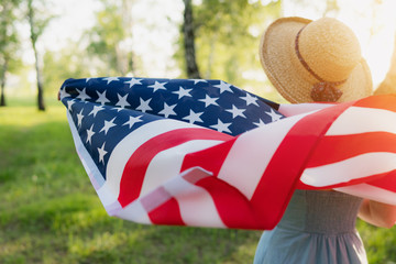 Closeup back view of a Proud woman enjoying summer sunset outdoors and holding american flag.