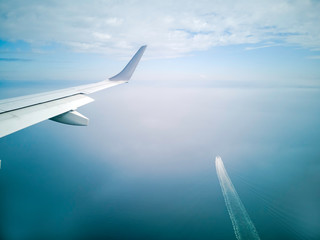 wings of the plane during the flight look from the passenger window. There are not many white clouds in the blue sky above the ground, overlooking the sea of Japan and the boat below.