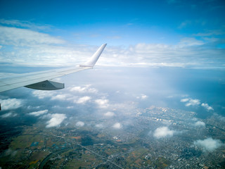 Fototapeta premium The wings of the plane during the flight look from the passenger window. There are white clouds in the blue sky.