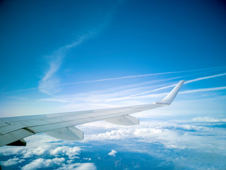 The wings of the plane during the flight look from the passenger window. There are white clouds in the blue sky.
