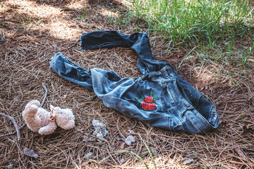 Old dirty female jeans in the woods with teddy bear on the ground.