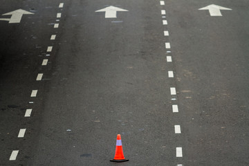Orange traffic cone standing between lanes of an avenue. Copy space