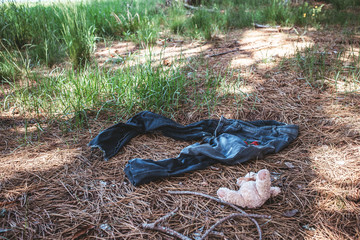Old dirty female jeans in the woods with teddy bear on the ground.
