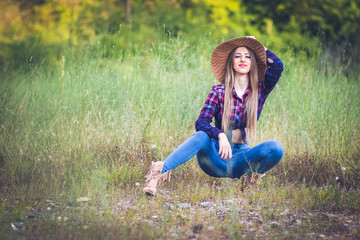 Fototapeta premium Cowgirl in jeans and checkered shirt posing in provocative pose in the nature