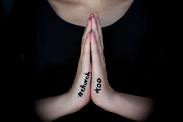 Woman holding hands in prayer with hashtag #churchtoo written on hands to protest the cover up of sexual assault in churches