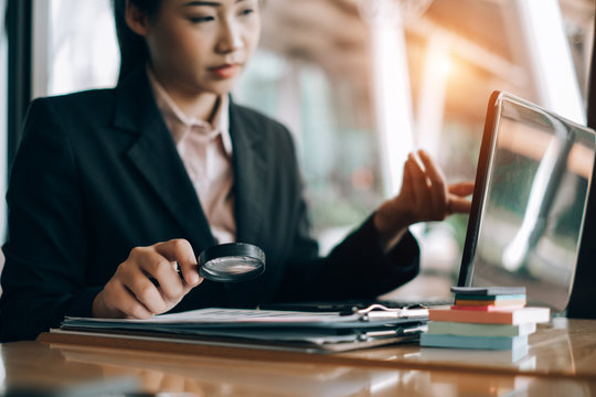 business woman smiling using a magnifying glass search analyzing investment graph at the office, investment concept