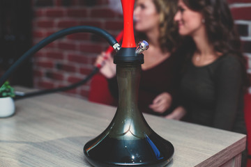 View of Hookah with candles and smoke on a table, hookah lounge with young people smoking in the background, shisha party club concept