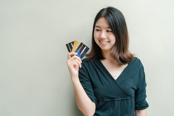 Asian beautiful woman Wearing a black shirt Have a credit card in hand Happy face Standing in the gray wall