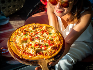 Woman showing tasty sliced pizza with seafood and tomato on wooden pizza board