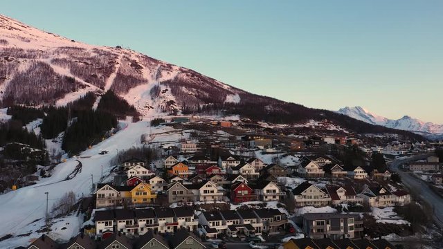 Aerial view of mountain in sunset with ski slope close to a city. A lot of houses in row. MOVING FORWARD.