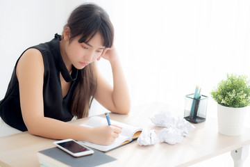 Obraz na płótnie Canvas Beautiful asian woman tired and stressed with writing overworked at desk, girl with worried not idea with notebook and crumpled paper at office, freelance and business concept.