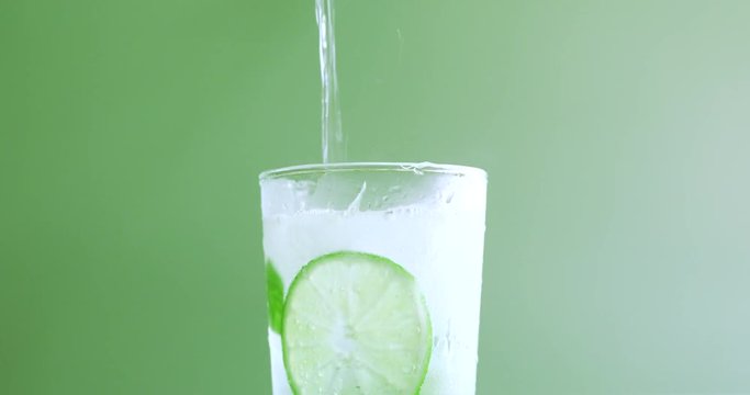 Pouring sparkling water in glass cup with slices of lime, sugar and rum to make Mojito Cocktail 