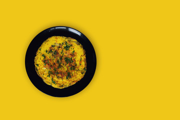 Herbal omelette in a black plate isolated on a yellow background