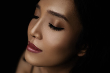 Fototapeta premium beautiful young woman closeup face closing eye and glossy healthy skin under glamour low key and makeup concept