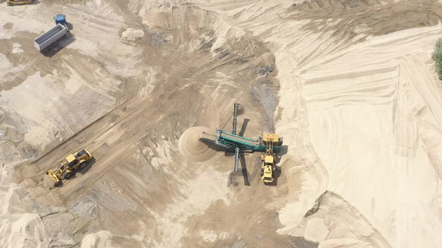 Top aerial view of bulldozer loading sand into empty dump truck in open air quarry.