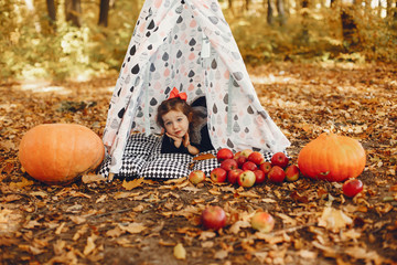 Cute child in a autumn park. Elegant little lady with pumpkins