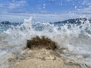 Closeup with splashing silky smooth swash water over a single rock into the seashore in Kota...