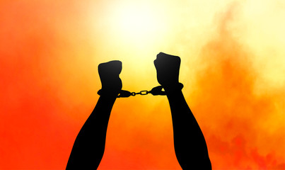 Silhouette of hands in handcuffs with sunset background