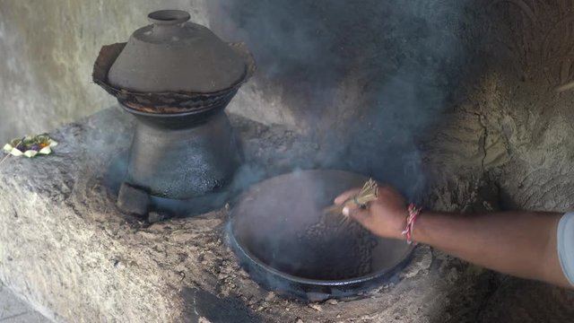 Old man roast coffee grains in an earthenware pot on fire in a local Balinese house, Ubud, island Bali, Indonesia. Roasted coffee beans in clay pot on the kitchen