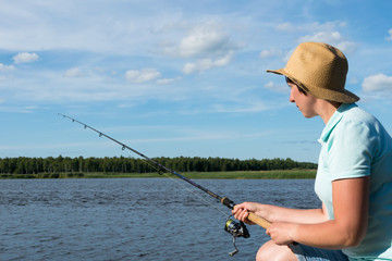 girl with a hat is fishing on a spinning on the river in good weather, close-up