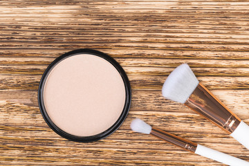 powder to equalize the tone of the face and two brushes lie on a burnt wooden background