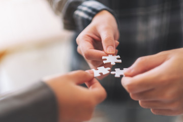 Closeup image of many people hands holding and putting a piece of white jigsaw puzzle together