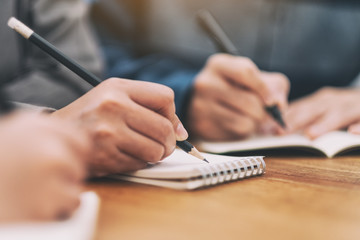 Closeup image of many people writing on blank notebook together on wooden table