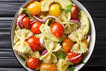 Italian pasta salad farfalle with ripe avocado, onions and tomatoes closeup in a bowl. horizontal top view