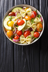 Pasta Farfalle with ripe avocado, onions and tomatoes close-up in a bowl. Vertical top view