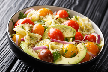 Pasta farfalle with ripe avocado, onions and tomatoes with spicy sauce closeup in a bowl. horizontal