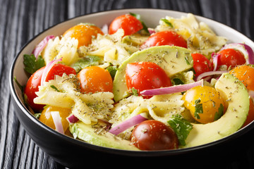 Appetizer Farfalle pasta salad with ripe avocado, onion and tomato closeup in a bowl. horizontal
