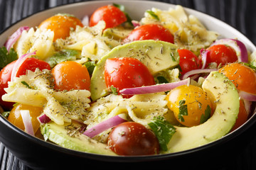 Farfalle pasta salad recipe with ripe avocado, onions and tomatoes closeup in a bowl. horizontal