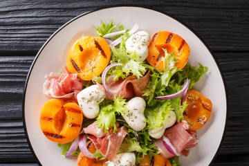 Delicious romantic salad with mozzarella, ham, apricot grilled and fresh lettuce close-up on a plate. horizontal top view