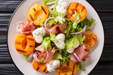 Italian salad with mozzarella, prosciutto, grilled apricots, red onion and  lettuce close-up on a plate. horizontal top view