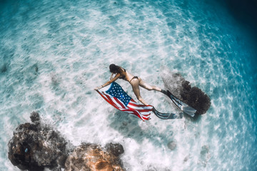 Beautiful woman freediver glides over sandy sea bottom with United States flag. Independence day.