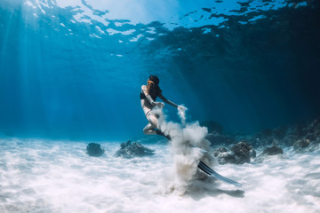 Woman freediver with white sand glides over sandy sea with fins. Freediving underwater in Hawaii