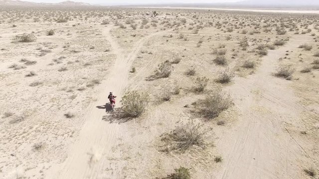 AERIAL: A dirt biker races on his Honda CRF motorcycle in the desert. Follow/tracking shot.