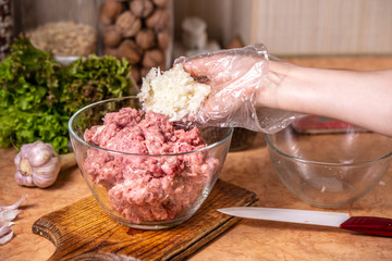 Hand puts chopped onion in a plate with minced meat.