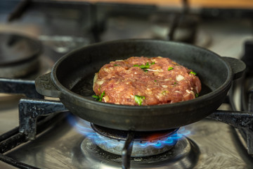 Iron pan with raw cutlet on a gas stove.