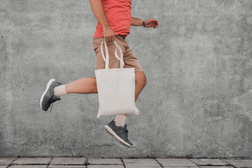 Young man is jumping with white cotton bag in his hands. Mock-up.