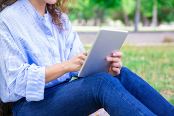 Close-up of woman using digital tablet in summer park. Unrecognizable student reading online book on gadget. Internet app concept