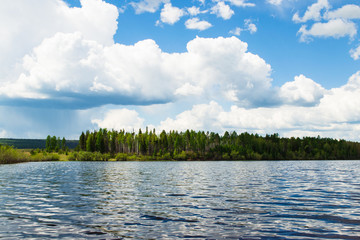 Lake on a sunny day, before the rain. The sky with thick clouds and coniferous forest