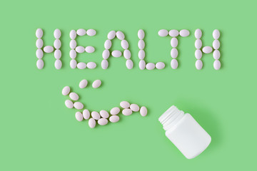 White pills in shape of word health and bottle on green background. Medical pharmacy concept....
