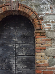 Antique door with wooden plank panels of a rural house, with iron fixing parts, Italy.