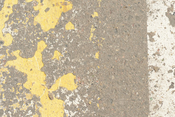Old asphalt surface with yellow paint on it close up. Abstract background
