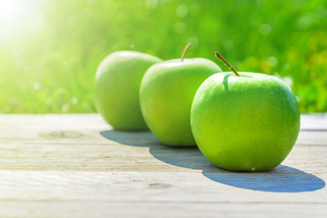 Freshly cropped geen apples on wooden table over grenn grass background.