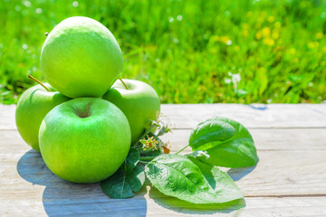 Freshly cropped geen apples on wooden table over grenn grass background.